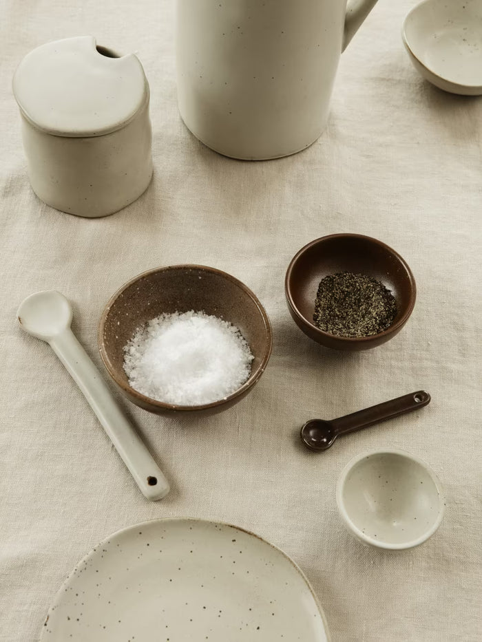 Collection of ceramic kitchenware including bowls, a plate, and measuring spoons on a textured surface.