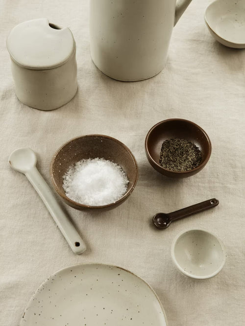 Collection of ceramic kitchenware including bowls, a plate, and measuring spoons on a textured surface.