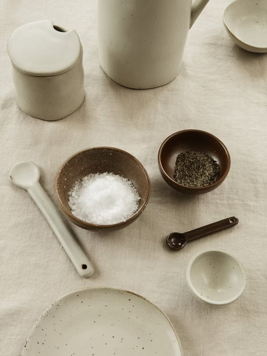 Collection of ceramic kitchenware including bowls, a plate, and measuring spoons on a textured surface.