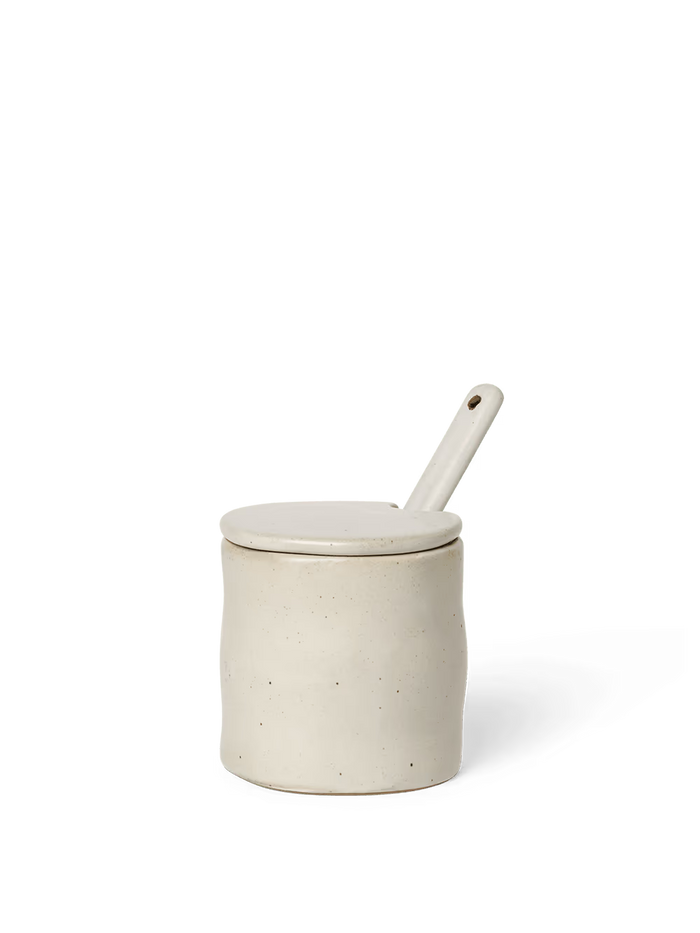 White ceramic jar with a lid and spoon on a black background