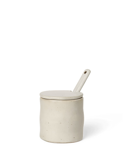White ceramic jar with a lid and spoon on a black background