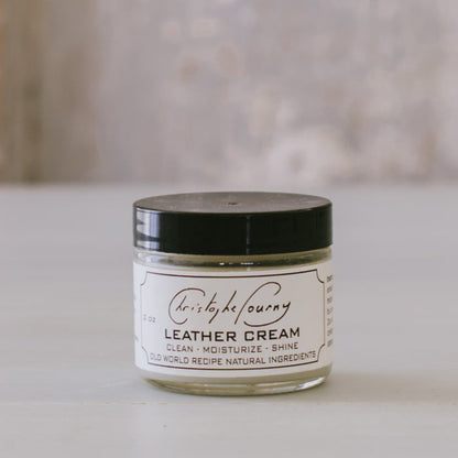 A 2oz glass jar of Leather Cream by Christophe Pourny Ltd., with a black lid, placed on a light surface.