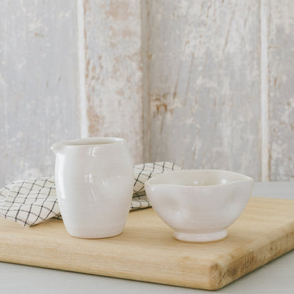 Two white stoneware bowls with white glaze on a wooden surface, with a checkered napkin in the background.